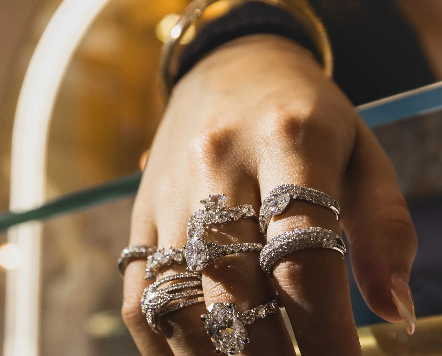 A hand wearing six diamond rings, including an oval solitaire and pavé bands, in the Asmar Jewelz showroom